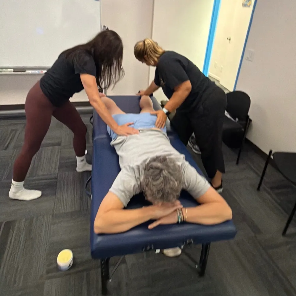 Yodi Richeson guiding a student's hands on a client lying face down on a treatment table