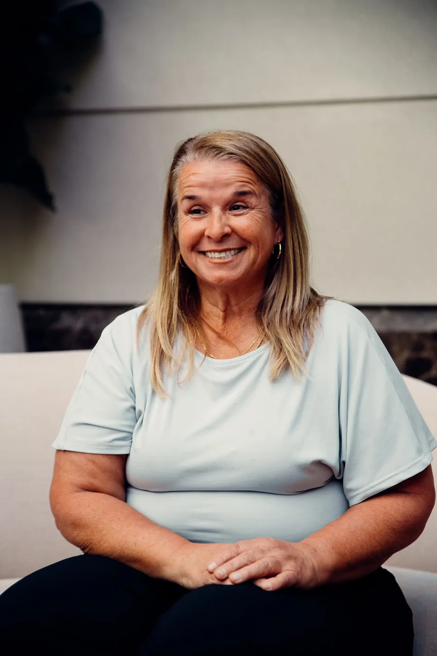 Yodi Richeson smiling, seated on a cream sofa with her hands folded
