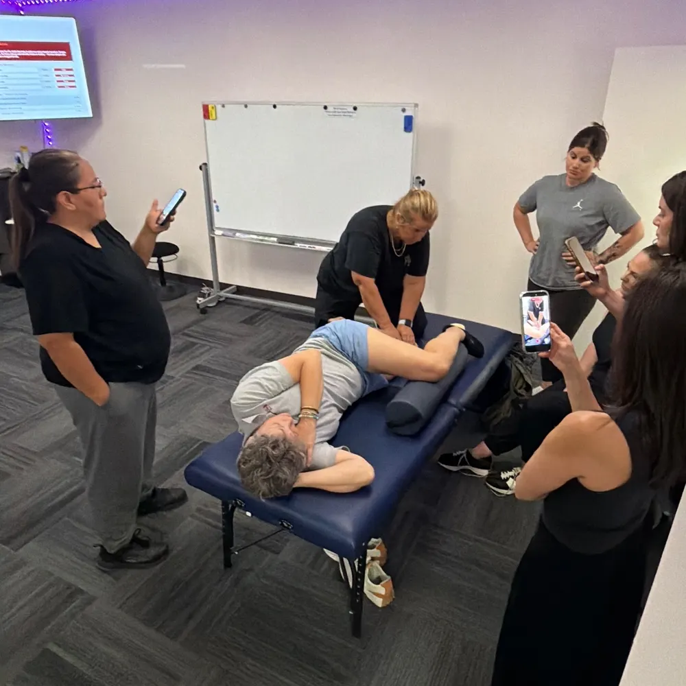Yodi Richeson working on a client's hip while a group of practitioners stands around the table watching