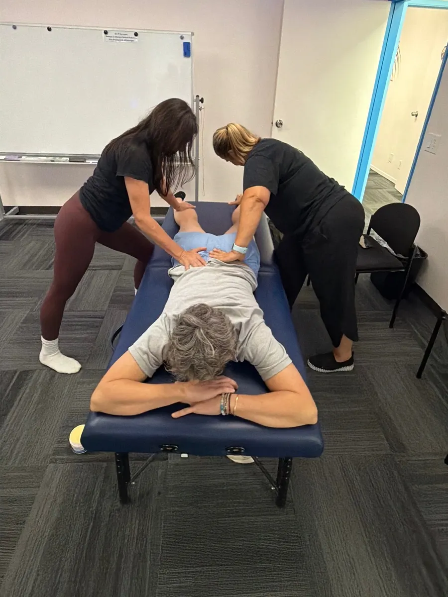 Yodi Richeson and a practitioner working side by side on a client's back in a training room