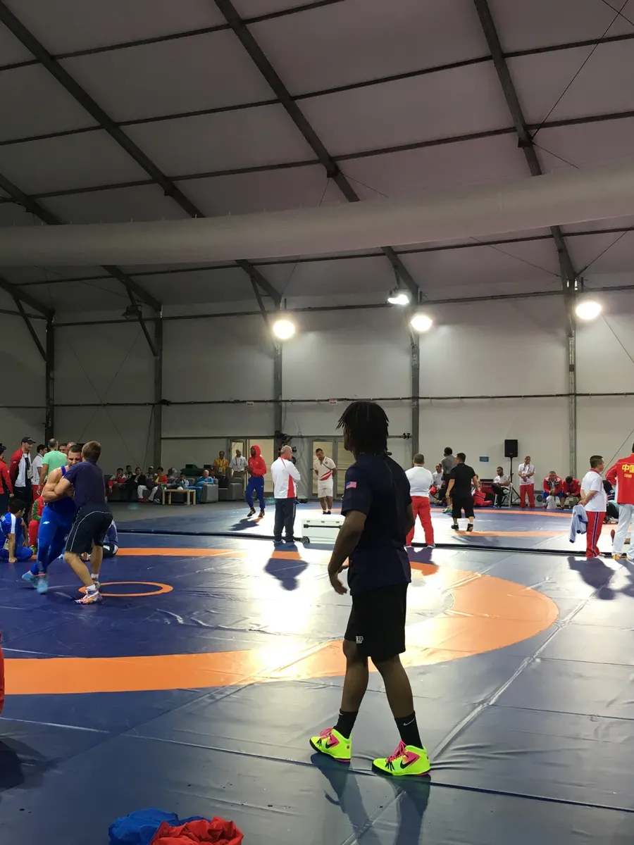 Athletes and team staff around wrestling mats in a large training hall